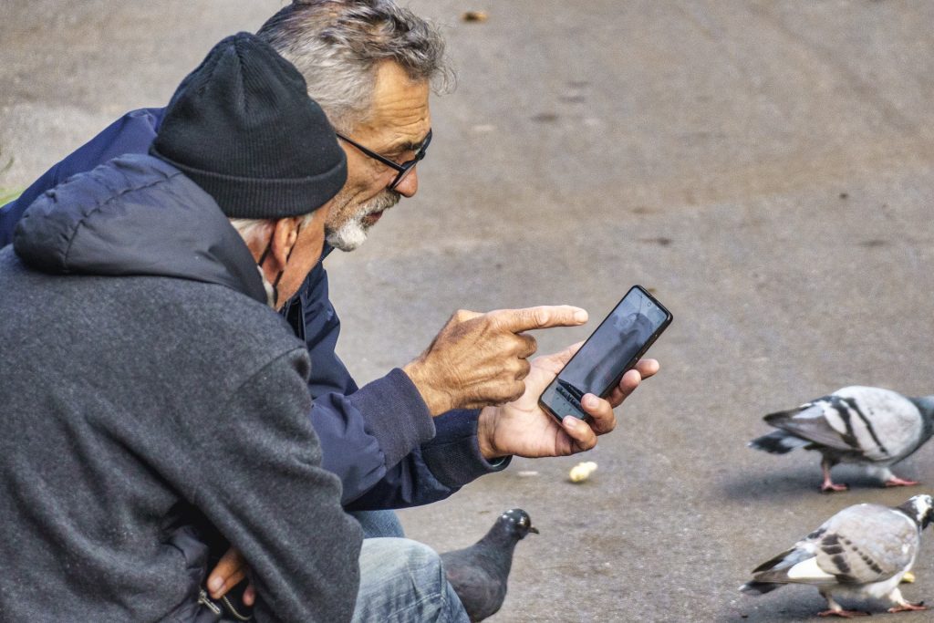 Starsi mężczyźni ze smartfonem robią zdjęcia gołębiom.